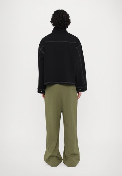Black jacket with visible stitching details and a high collar, paired with loose-fitting olive green trousers featuring subtle seams.