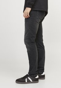 Jeans de mezclilla negros con un ajuste slim, diseño de cinco bolsillos y una textura ligeramente deslavada. Combinados con zapatillas negras con toques blancos.