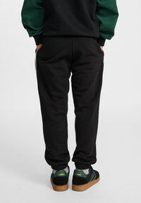 Czarne dresowe spodnie z elastycznymi mankietami, w połączeniu z czarno-zielonymi sneakersami z gumową podeszwą i logo marki na pięcie.