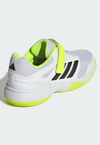 Scarpa sportiva bianca con strisce nere e dettagli verde neon. Presenta una parte superiore in mesh, una linguetta in Velcro e una suola testurizzata per una maggiore aderenza.