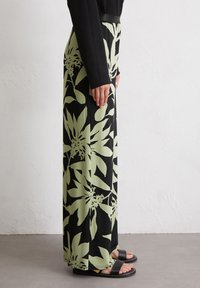Flowy, black pants with large light green floral pattern; made of smooth fabric, featuring a wide leg and a fitted waistband.