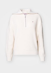 Kardigan z prążkowanego materiału w kolorze off-white z kołnierzem na ćwierć zamka i małym logo w kolorach czerwonym, białym i niebieskim na piersi.