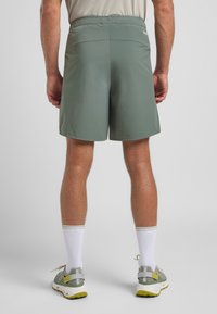 Shorts pour hommes en tissu vert atténué, dotés d'une taille élastique et d'un design minimaliste. Texture lisse, coupe au genou, sans motifs visibles.