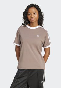 Hnedé tričko s krátkym rukávom a bielymi lemovkami na golieri a rukávoch, s malým logom Adidas na hrudi a športovými bočnými pruhmi.