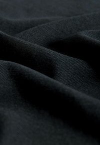 Černá texturovaná tkanina s měkkým, hladkým povrchem, vykazující jemné záhyby a variace ve stínování, které naznačují její pružný materiál.