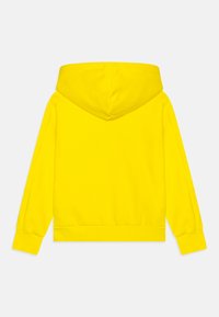 Sudadera amarilla con capucha, que presenta una textura suave, mangas largas y puños de canalé. El diseño es simple, sin logotipos ni patrones visibles.