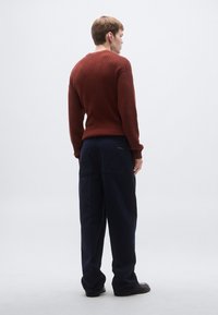 Κόκκινο ριγέ πουλόβερ με στρογγυλή λαιμόκοψη, φορεμένο με ναυτικό ευρύχωρο παντελόνι. Σημαντικές λεπτομέρειες είναι τα μανίκια με μανσέτες και οι πλαϊνές τσέπες. Μαύρα παπούτσια.