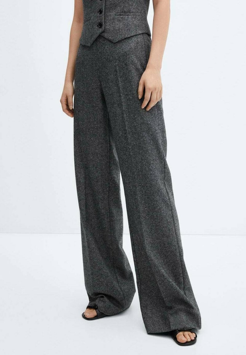 Pantalon gris à jambes larges porté avec un gilet assorti, associé à des sandales noires à bout ouvert, présenté sur une personne debout sur fond blanc.