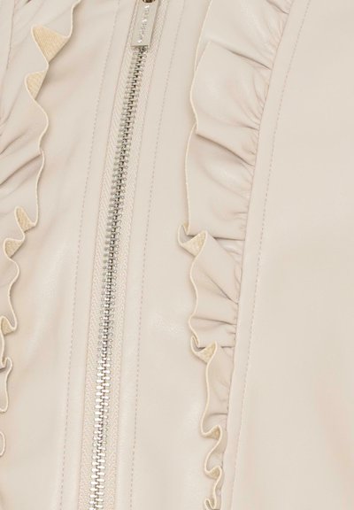 Vêtement en cuir couleur crème avec une fermeture éclair centrale en argent et des détails froncés doux de chaque côté de la fermeture éclair.