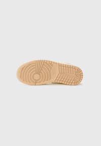 Semelle de chaussure en matériau caoutchouté. Couleur beige clair, dotée d'un motif de semelle pour l'adhérence et d'un logo circulaire près du centre.