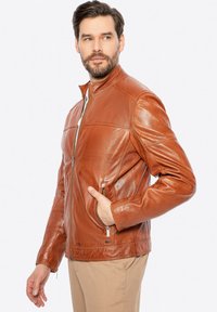 Giacca in pelle marrone con colletto alto, zip frontale e tasche laterali. Presenta dettagli cuciti e una texture liscia e lucida.
