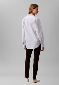 Hvit og lys blåstripet langermet skjorte med krage, buet kant, kombinert med svarte smale bukser og beige flate sko.