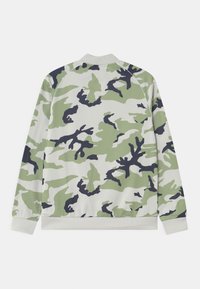 Chaqueta de manga larga con puños y cuello acanalados, que presenta un patrón de camuflaje verde, negro y blanco en la parte trasera.
