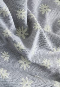 Tejido de punto gris claro con un patrón floral que presenta margaritas de color crema, mostrando una textura suave y un fino detalle.