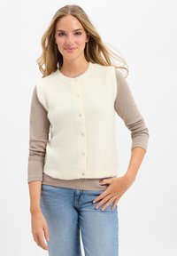 Weißer, gestrickter Pullunder mit Rippstruktur und rundem Ausschnitt, mit Knopfleiste und ärmellosem Design, getragen über einem beigefarbenen Langarmshirt.