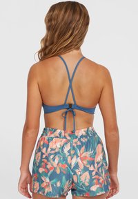 Haut de bikini bleu avec bretelles ajustables, associé à un short de bain floral à taille élastique présentant des motifs roses et verts sur un fond bleu.