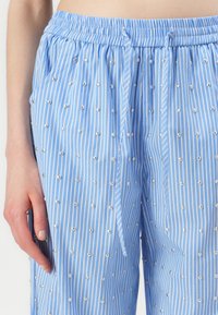 Lichtblauwe gestreepte broek met elastische taille, voorzien van kleine zilveren stippen die gelijkmatig over de stof zijn verspreid, wat textuur en contrasterende elementen creëert.