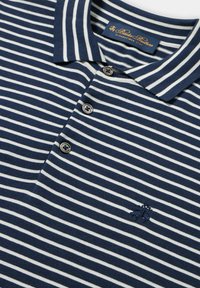 Polo tričko v námořnické modré a bílé pruhované barvě vyrobené z měkké látky, s klasickým límečkem, tříknoflíkovým zapínáním a vyšitým logem.