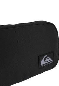 Borsa in tessuto nero con superficie testurizzata. Presenta un'etichetta con il logo grigio di Quiksilver. Forma rettangolare con chiusura a zip sulla parte superiore.