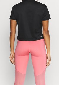 Černé krátké tričko s hladkou texturou a krátkými rukávy, doplněné růžovými legínami s průhlednými panely a přiléhavým střihem.