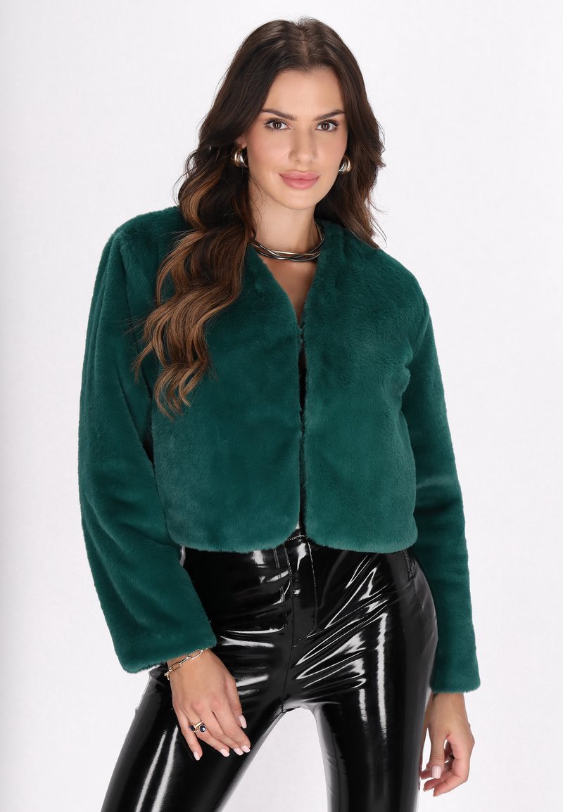 Teal faux fur jakke med cropped design og brede ærmer, parret med højt shine sorte leggings, der fremhæver en tætsiddende silhuet.
