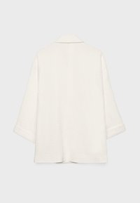 Veste ample de couleur blanc cassé avec des manches larges, un petit col et un ourlet droit, montrée de dos sur un fond uni.