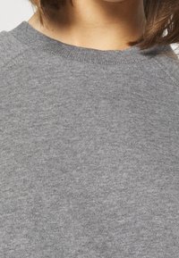 Suéter gris de punto con cuello redondo, que presenta una tela de punto lisa y texturizada. Mangas raglán y sutiles detalles de costura.