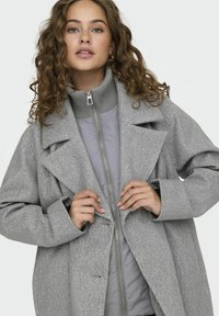 Cappotto grigio in misto lana con colletto a revers, silhouette strutturata e giacca interna grigia con zip. Caratterizzato da maniche ampie e texture morbida.