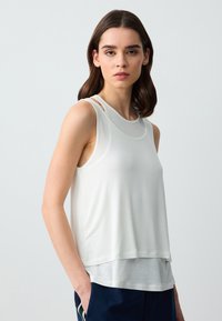 Top bianco senza maniche con un design a strati, caratterizzato da un collo rotondo e inserti a taglio sulle spalle. Texture liscia, vestibilità casual.