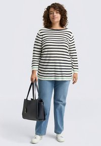 Gestreiftes Langarmshirt in Creme mit schwarzen Streifen, kombiniert mit hellblauen Jeans und einer schwarzen Handtasche, getragen mit weißen Turnschuhen.
