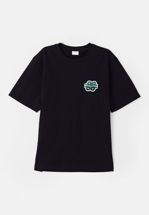 Musta puuvillainen T-paita lyhyillä hihoilla, jossa on vihreä brodeerattu logo vasemmassa rinnassa ja klassinen pyöreä kaula-aukko.
