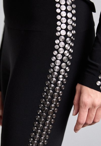 Sorte leggings med en vertikal række af sølvmetalliske nitter langs den ene side, med en glat, strækbar tekstur og tætsiddende design.