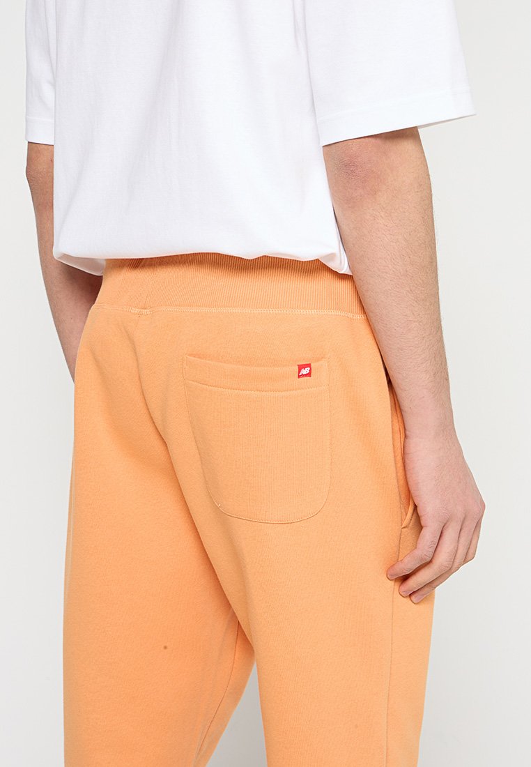 Pantalones de chándal naranjas con una cinturilla acanalada, que incluyen un bolsillo trasero y una pequeña etiqueta de logotipo roja en la parte superior derecha. Material suave de mezcla de algodón.