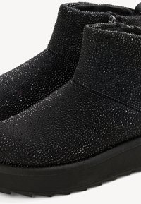 Bottes noires jusqu'à la cheville avec un design texturé, mettant en avant des accents scintillants, un bout arrondi et une semelle noire robuste avec une légère plateforme.