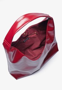Sac fourre-tout en cuir rouge avec une large ouverture, texture lisse et intérieur en tissu bordeaux avec une poche zippée. Design minimaliste.
