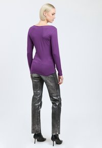 Langärmliges lila Oberteil mit Rundhalsausschnitt, kombiniert mit metallischen silbernen Skinny-Hosen und schwarzen Stiefeletten, von hinten betrachtet.