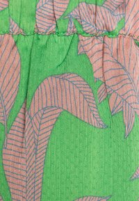 Tissu vert avec un motif de feuilles ; les feuilles sont roses avec des lignes bleues. La surface texturée et les fronces créent un effet de superposition.
