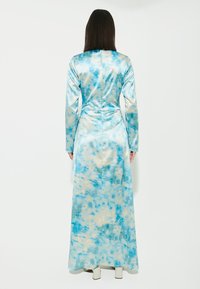 Lungo abito blu in satin con un motivo simile a delle nuvole in toni più chiari, con maniche lunghe e una silhouette aderente.
