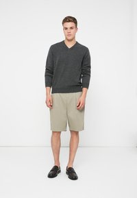 Pull gris à col en V en maille, associé à un short beige. Le mannequin porte des baskets noires sans lacets. Design simple et épuré, avec des couleurs neutres.
