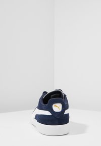 Marineblaue Wildledersneaker mit weißen Akzenten, niedriges Design, gepolsterte Manschette und gelbes Logo an der Ferse. Gummisohle.