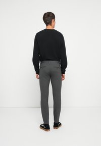 Suéter negro texturizado, pantalones gris ajustados, vista trasera. Los pantalones tienen bolsillos traseros; los zapatos son negros con acentos blancos y suelas marrones.