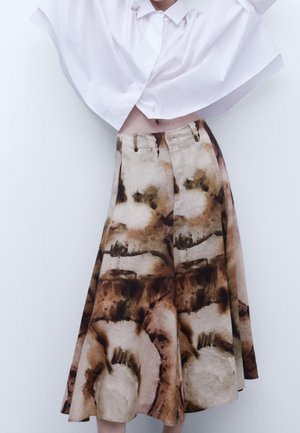 Biała krótka koszula na guziki noszona z wysokim stanem i szerokimi spodniami z abstrakcyjnym brązowo-beżowym wzorem tie-dye.