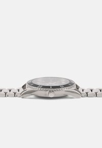 Sølv rustfrit stål ur med sort urskive, ensidig drejbar bezel og en glat metalarmbånd. Udstyret med en krone og dekorative accentdetaljer.