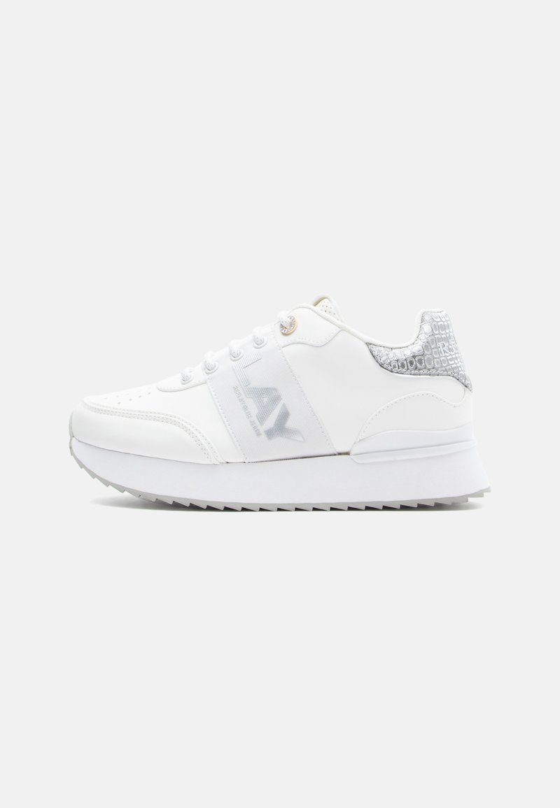 Λευκό αθλητικό παπούτσι με υφασμάτινη ασημί λεπτομέρεια στη φτέρνα, διάτρητο σχέδιο στο μπροστινό μέρος και έντονο λογότυπο στο πλάι. Επίπεδη σόλα με αντοχή στην ολίσθηση.