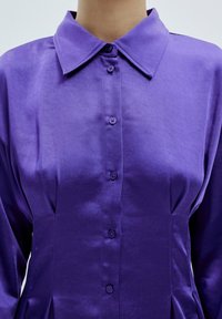 Lila Satinbluse mit klassischem Kragen, durchgehender Knopfleiste und langen Ärmeln. Verfügt über einen dezenten Glanz und eine taillierte Taille mit Faltendetails.