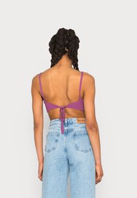 Bralette tricotado roxo com alças finas, atado nas costas; combinado com jeans de ganga azul claro de cintura alta com bolsos.