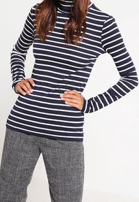 Maglione a collo alto a righe blu navy e bianche con maniche lunghe. Materiale morbido, design aderente, caratterizzato da un colletto alto e maniche slim. Abbinato a pantaloni neri e bianchi texture.