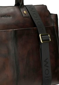 Brązowa skórzana torba o gładkiej fakturze, wyposażona w czarny, regulowany pasek z wytłoczonym logo oraz złotą metalową klamrę.