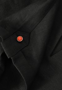Tissu noir avec un gros plan sur un poignet boutonné présentant un petit bouton rond orange avec un bord doré.
