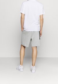 Vit t-shirt med rund krage, grå shorts med elastisk midja och vita sneakers med svarta accentfärger. Bakifrån, minimalistisk design.